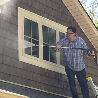 Crew member pressure washing the side of a brown shake-shingle house